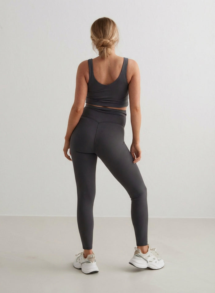 A woman seen from behind wearing Shadow Grey Sense Maternity Tights and a matching sports bra from aim'n.