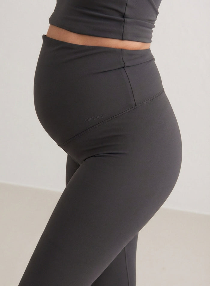 Side view of a pregnant woman wearing Shadow Grey Sense Maternity Tights by aim'n, featuring a high waistband that covers the belly.