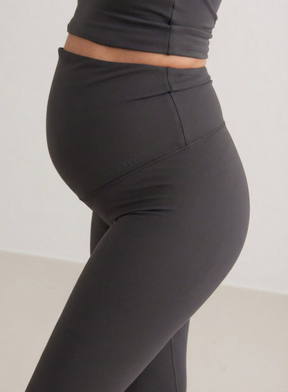 Side view of a pregnant woman wearing Shadow Grey Sense Maternity Tights by aim'n, featuring a high waistband that covers the belly.