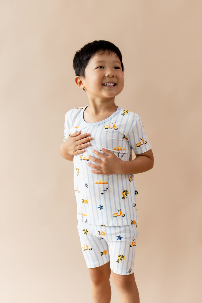Young boy posing wearing the Short Sleeve Pajamas in Amalfi Coast standing in front of a light taupe background