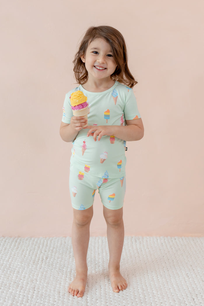 Child smiling holding an ice cream cone wearing short sleeve pajama set in Mint Ice Cream print on beige background