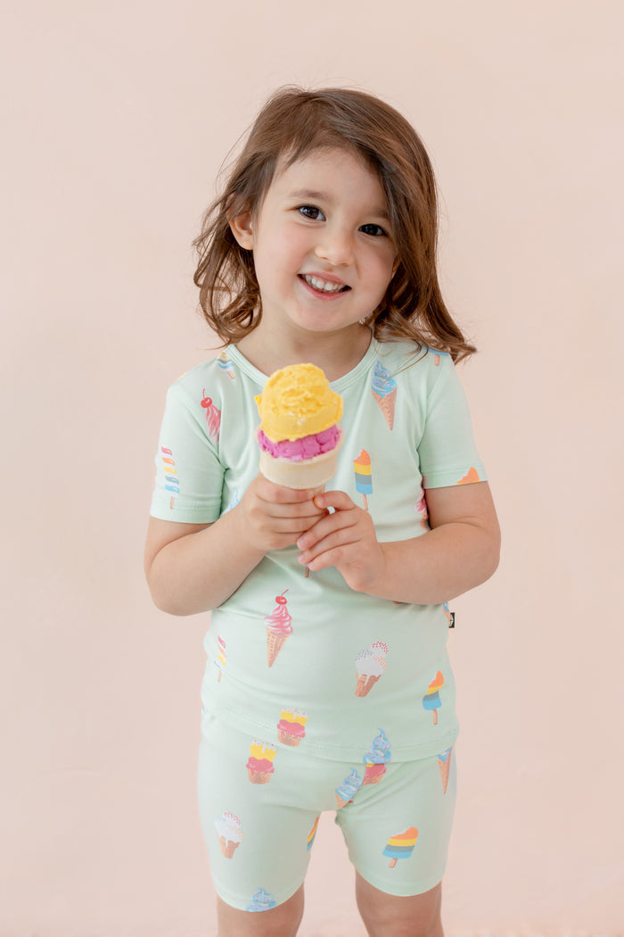 Child wearing short sleeve pajama set in Mint Ice Cream print smiling with an ice cream cone on a beige background