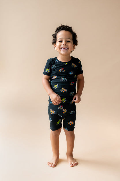 Boy wearing Black Short Sleeve Pajamas in Monster Truck print on beige background