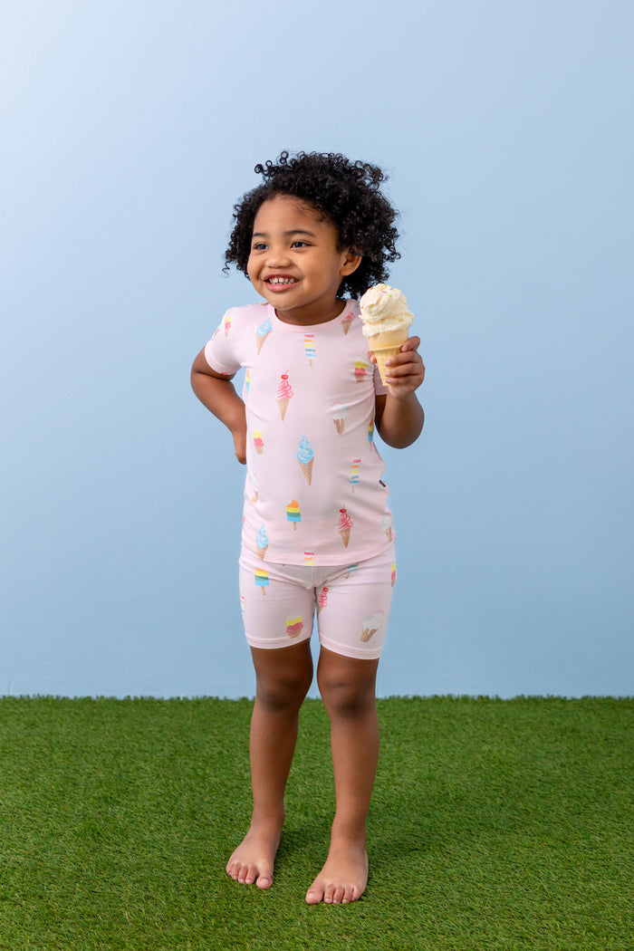 Child smiling with an ice cream cone wearing short sleeve pajama set in Sakura Ice Cream print on green grass