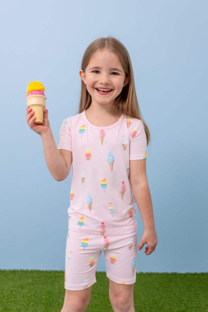 Child smiling with an ice cream cone wearing short sleeve pajama set in Sakura Ice Cream print on a blue background and green grass