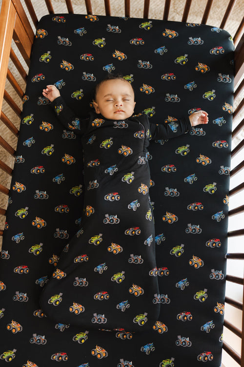 Baby sleeping in black Sleep Bag with Monster Truck print on similar print crib sheet.