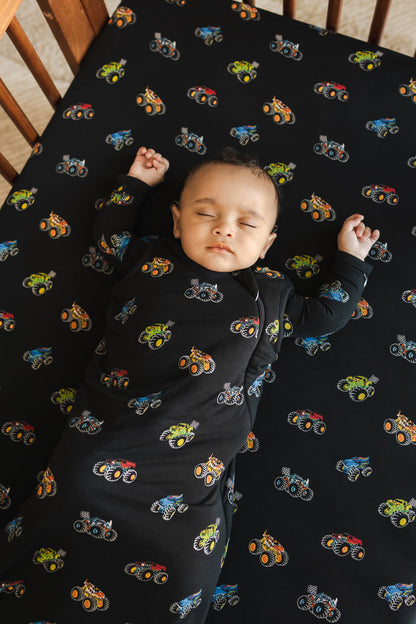 Baby wearing black Sleep Bag with Monster Truck print sleeping in a crib with similar print crib sheet.