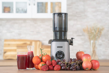 Der Unold Slow Juicer Sam steht auf einer Küchentheke, daneben Äpfel, Trauben, Tomaten und Erdbeeren. Neben den Früchten stehen zwei Gläser – eines voll und eines halbvoll mit rotem Saft.