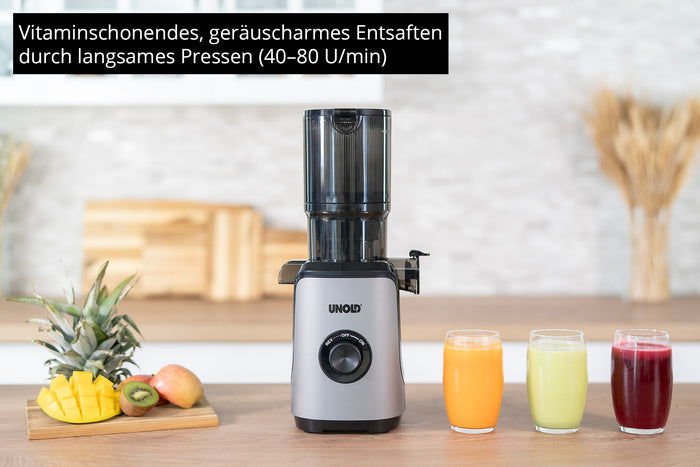 Der Unold Slow Juicer Sam in Silber und Schwarz steht auf der Küchentheke neben Ananas, Apfel, Orangen und drei Saftgläsern (grün, orange, rot). Der deutsche Text oben hebt die sanfte und leise Entsaftung hervor.