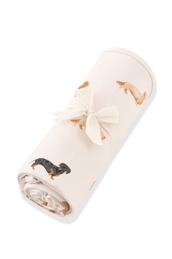 Beige Swaddle Blanket in Dachshund print rolled up in ribbon on a white background