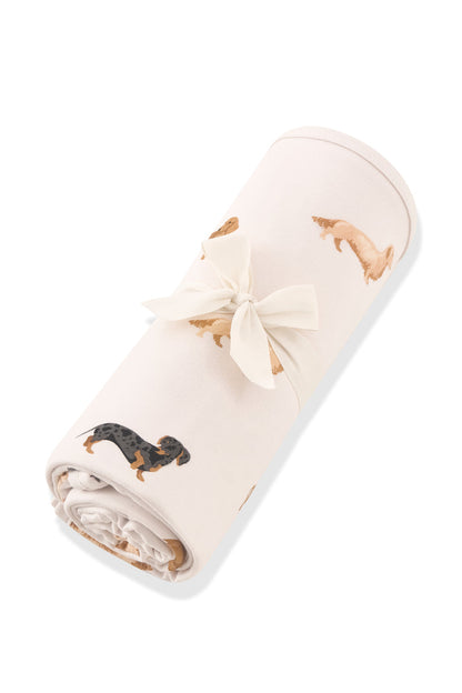 Beige Swaddle Blanket in Dachshund print rolled up in ribbon on a white background