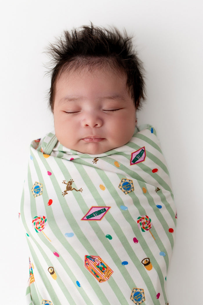 Baby in a green and white striped Swaddle blanket with colorful Harry Potter patterns on a white background