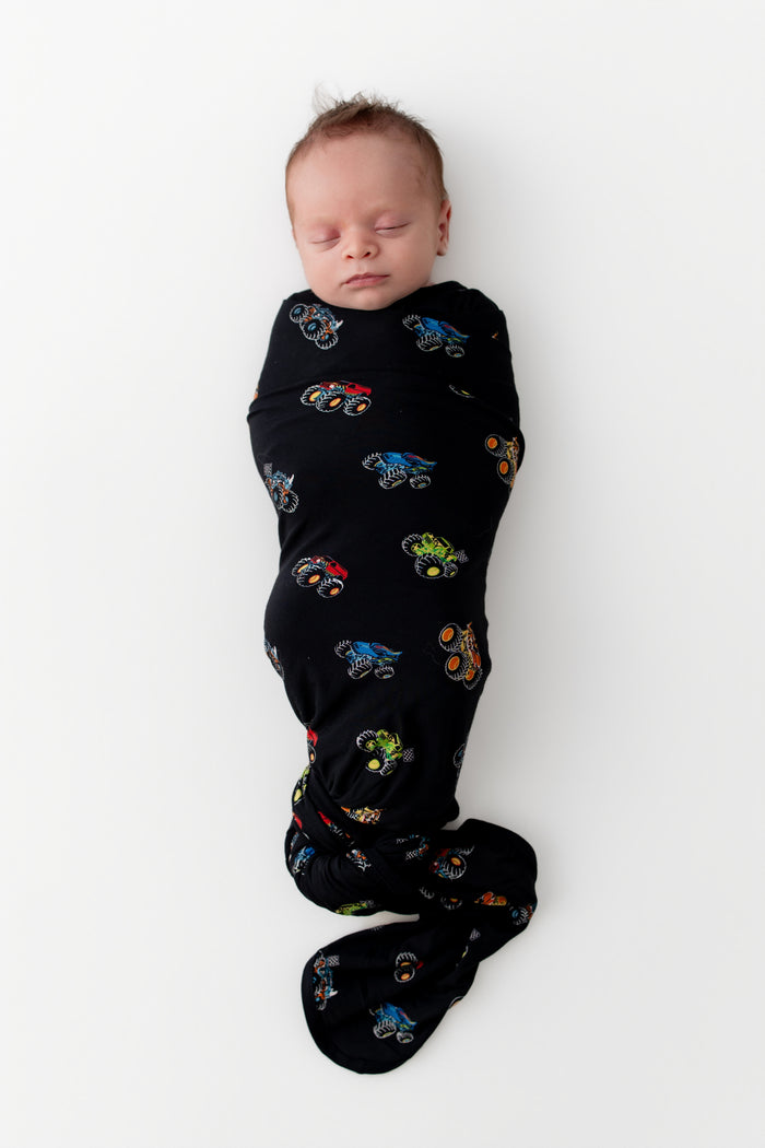 Baby sleeping in Black Swaddle Blanket in Monster Truck print on white background