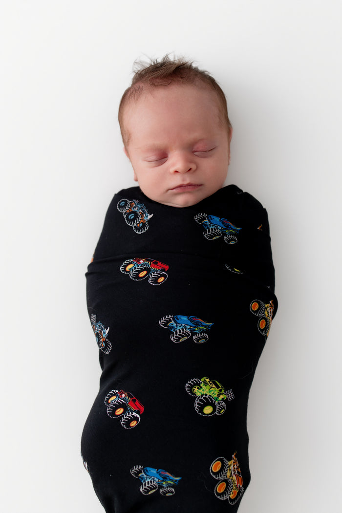 Baby sleeping in Black Swaddle Blanket in Monster Truck print on white background