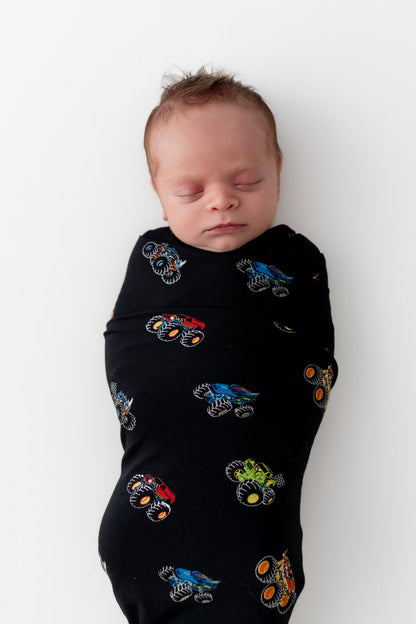 Baby sleeping in Black Swaddle Blanket in Monster Truck print on white background