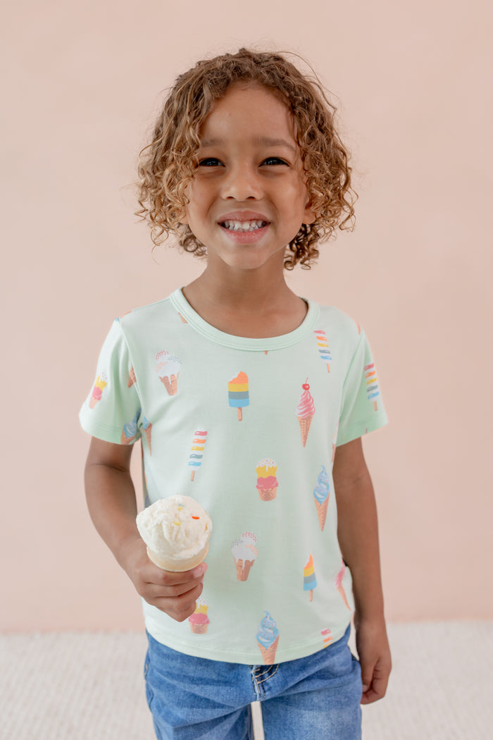 Child smiling holding an ice cream cone wearing Toddler Basic Tee in Mint Ice Cream over Denim pants print on a beige background