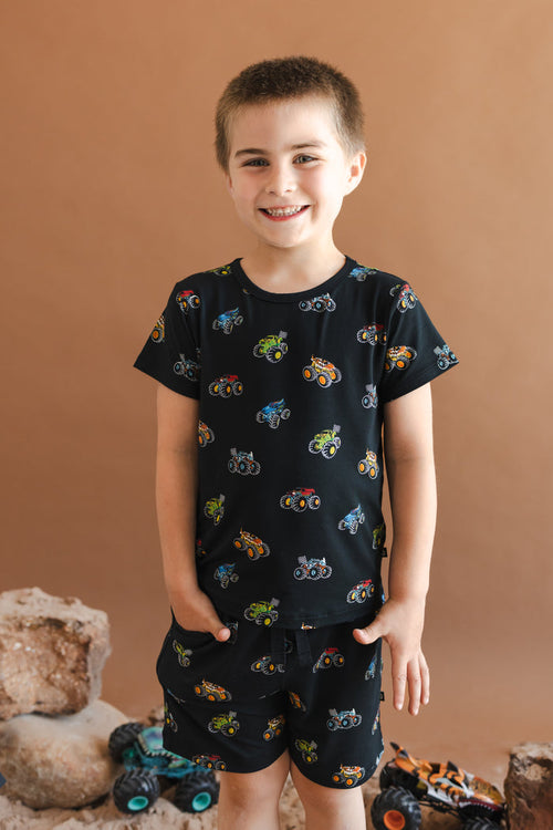 Boy wearing Black Toddler Basic Tee in Monster Truck print on beige background