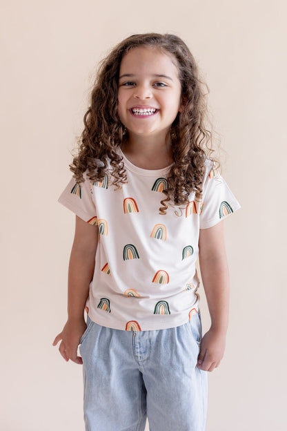Girl posing in Toddler Basic Tee in Retro Rainbow print over blue pants on a white background
