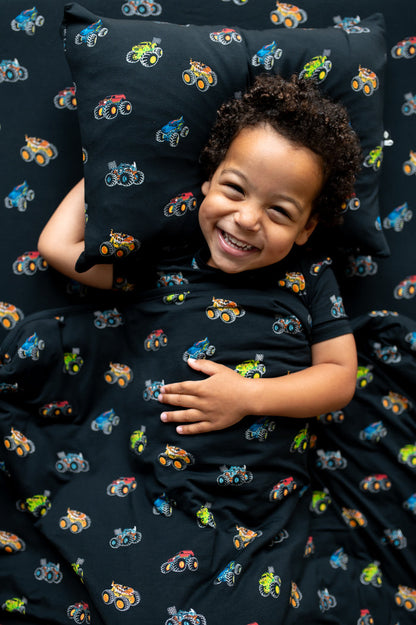 Boy lying on black Toddler pillowcase and sheet with Monster Truck print under a similar print Toddler blanket