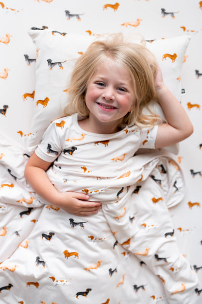 Girl lying on a Beige Toddler Pillowcase and beige sheet covered under a Beige Toddler Blanket with Dachshund print
