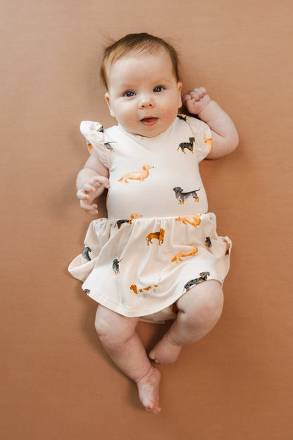 Baby in Beige Twirl Bodysuit Dress in Dachshund print on a brown background