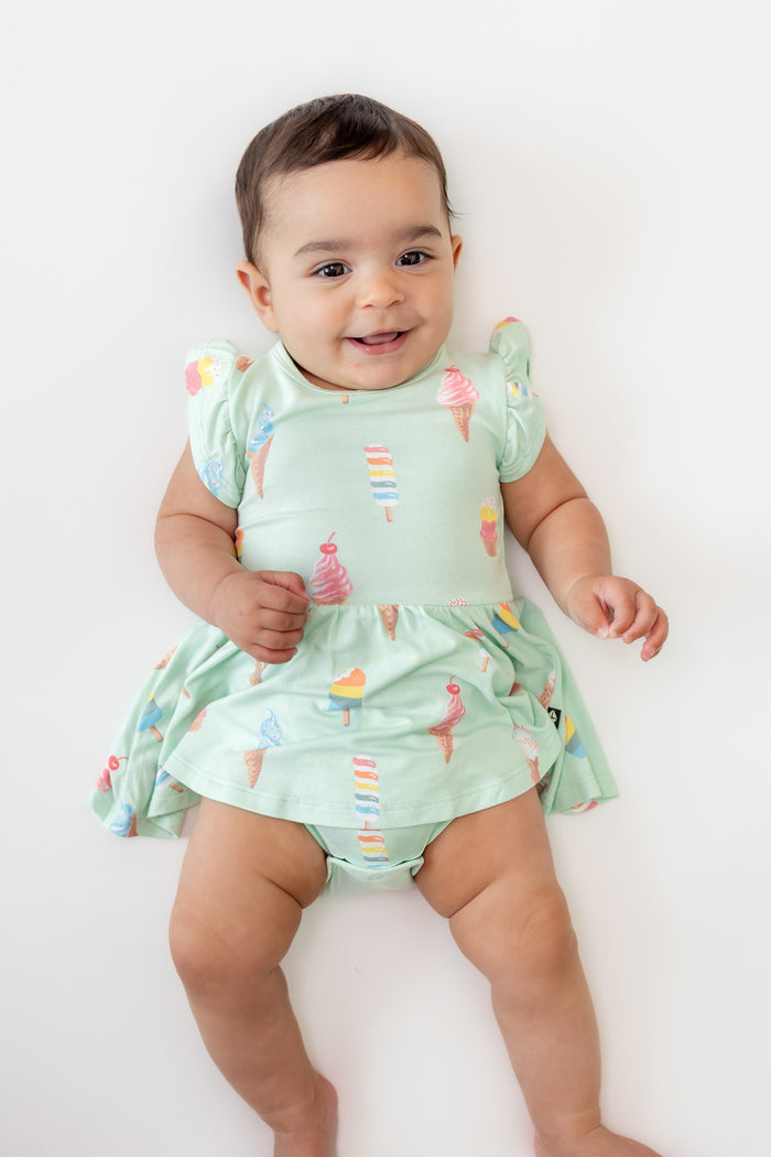 Baby wearing Twirl Bodysuit Dress in Mint Ice Cream print on a beige background