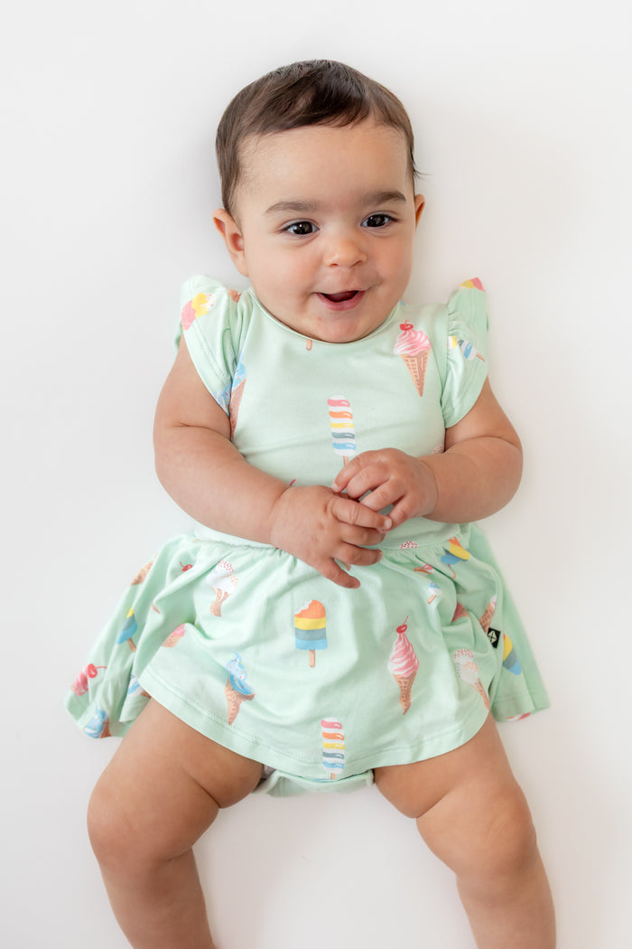 Baby posing in Twirl Bodysuit Dress in Mint Ice Cream print on a beige background
