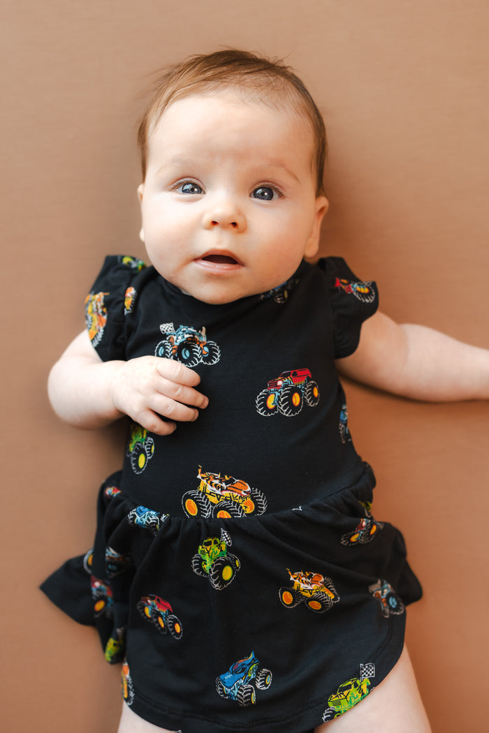 Baby in Black Twirl Bodysuit Dress in Monster Truck print on beige background