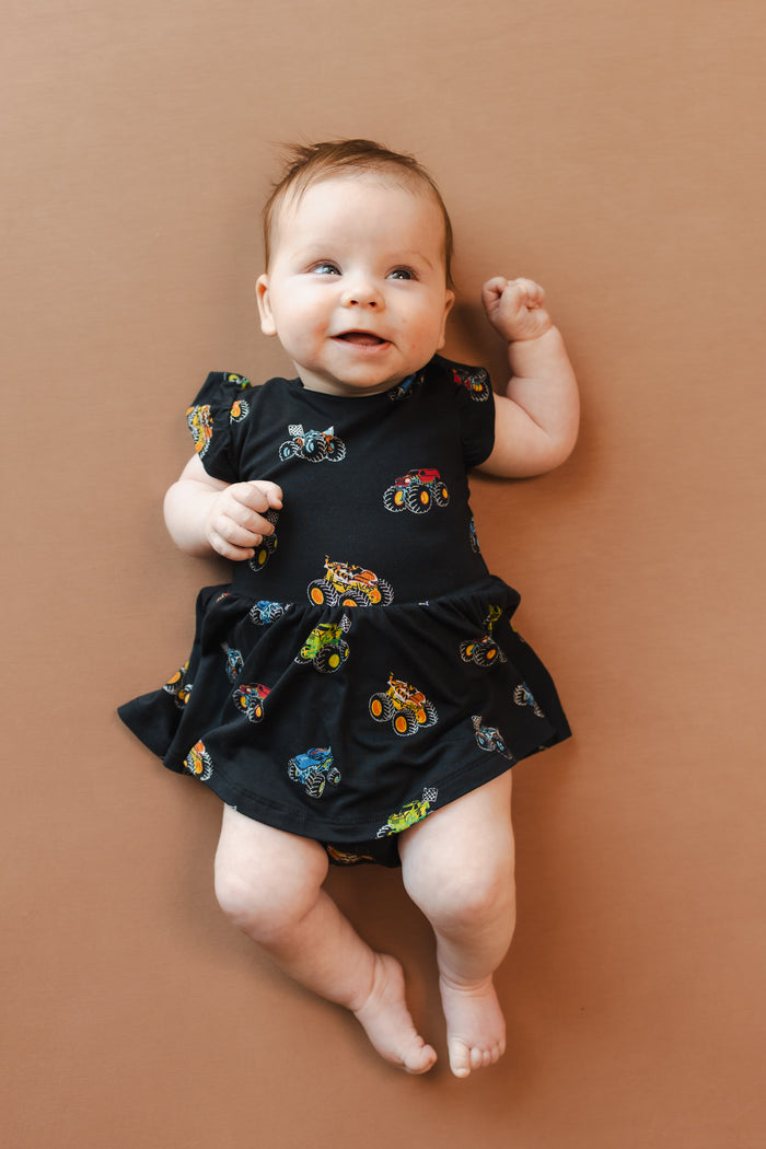 Baby smiling in Black Twirl Bodysuit Dress in Monster Truck print on beige background
