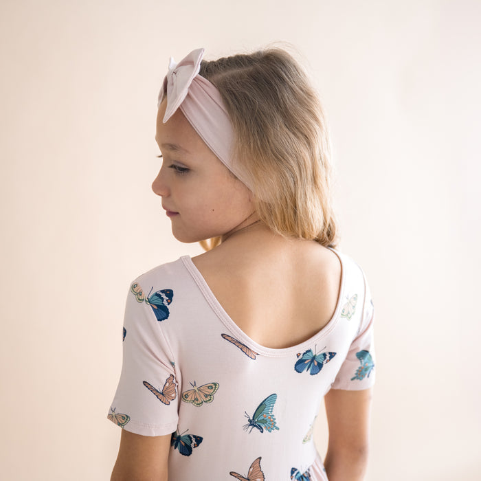Young girl wearing a pink dress with butterfly patterns and a headband on a plain background