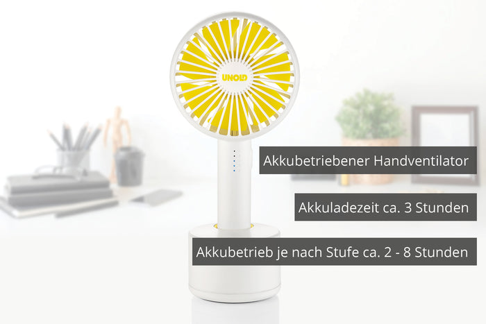 Auf dem Schreibtisch steht ein kompakter gelb-weißer Handventilator von Unold aus dem „Ventilatoren-Set Tischventilator Breezy Clip + Handventilator Breezy Swing“, der mit Akkubetrieb, 3-stündiger Ladezeit und je nach Geschwindigkeit 2–8 Stunden Betriebszeit überzeugt.