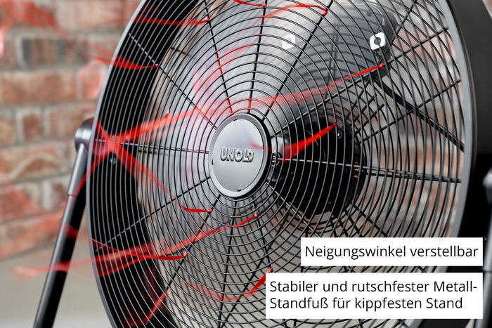Nahaufnahme des Unold Windmaschine Black Steel Standventilators mit roten Luftstromlinien, verstellbarer Neigung und einem stabilen, rutschfesten Metallsockel. Vor dem Hintergrund einer Backsteinmauer.
