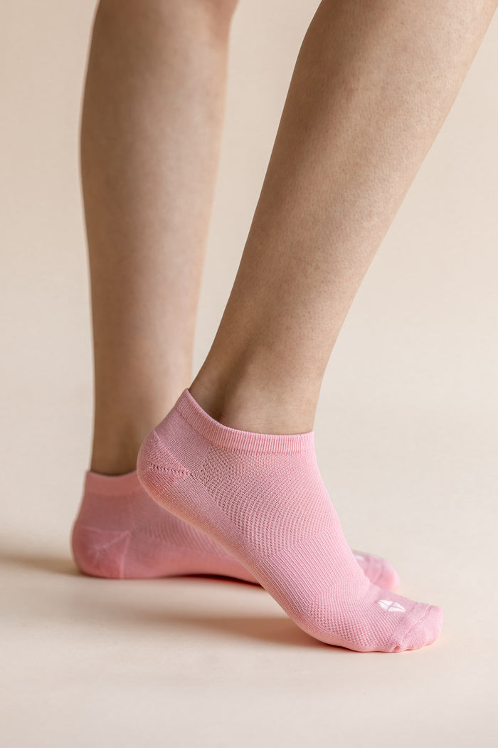 A close-up of a person's feet wearing light pink low-cut ribbed ankle socks against a solid pale beige background.