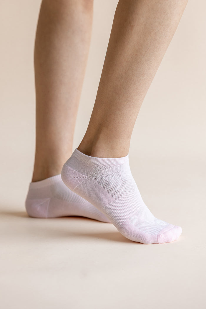 A pair of light pink low-cut ankle socks worn on a person's feet, shown against a solid, warm beige background.