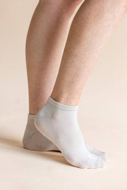 A close-up of a person's feet wearing light gray ankle socks against a solid beige background.