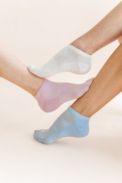 Three low-cut ankle socks in white, light pink, and light blue, shown on feet against a soft beige background.