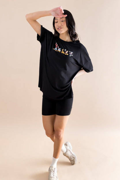 Woman wearing a black oversized t-shirt with mickey mouse graphics and black shorts on a beige background
