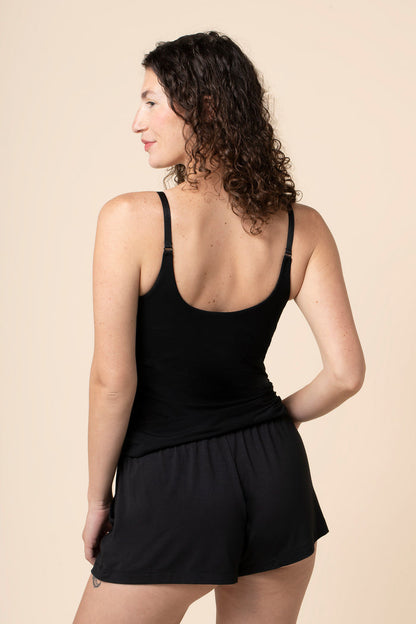 Woman wearing a black tank top and shorts against a beige background