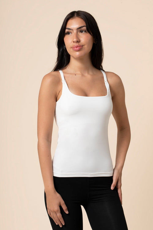 Woman wearing a white nursing tank top and black pants against a beige background