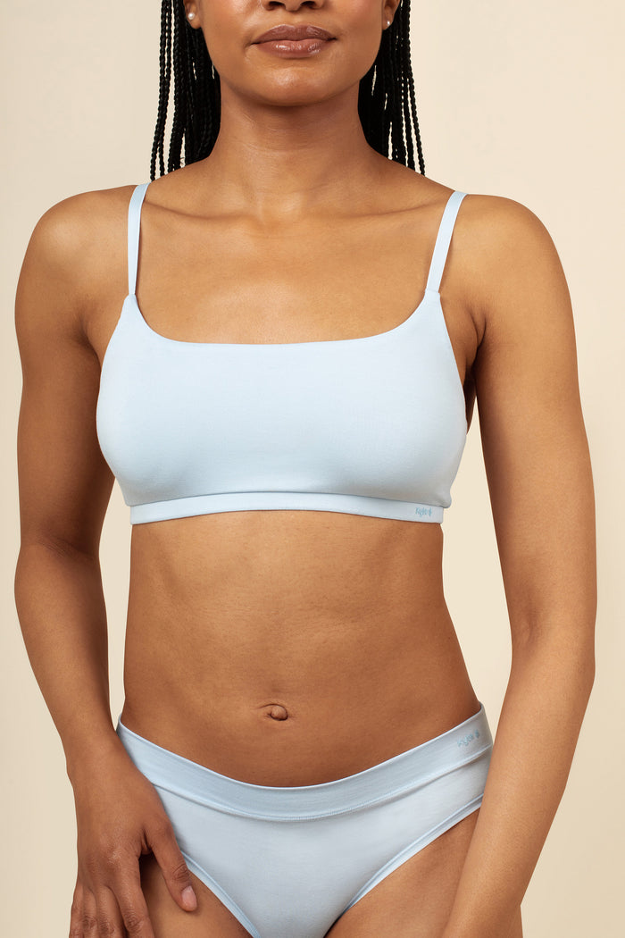 Woman wearing a light blue scoop bra set against a beige background