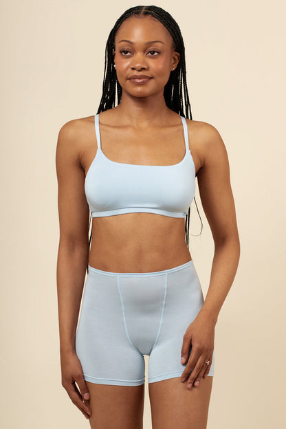 Woman wearing a light blue scoop neck bra and high-waisted boxer shorts on a beige background