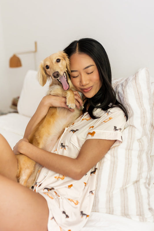 Woman wearing short sleeve pajamas with a wiener dog pattern holding her dachshund dog