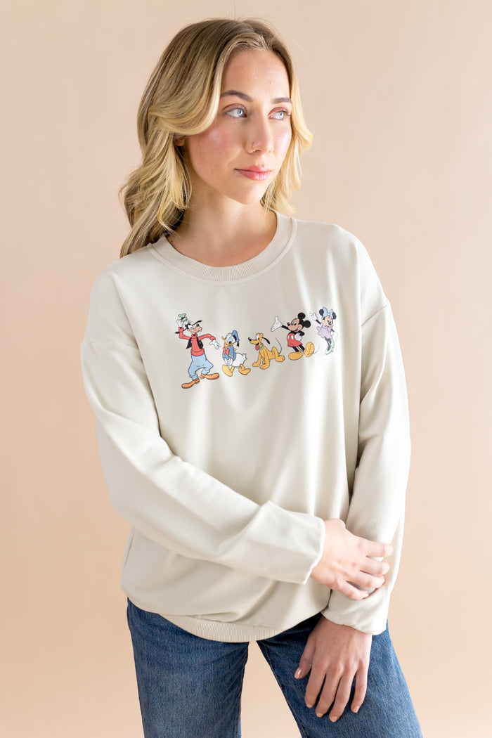 Woman wearing a cream sweatshirt with cartoon character design on a beige background