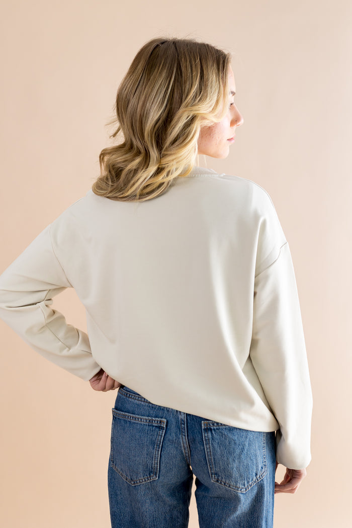 Woman wearing a beige sweater and blue jeans against a beige background