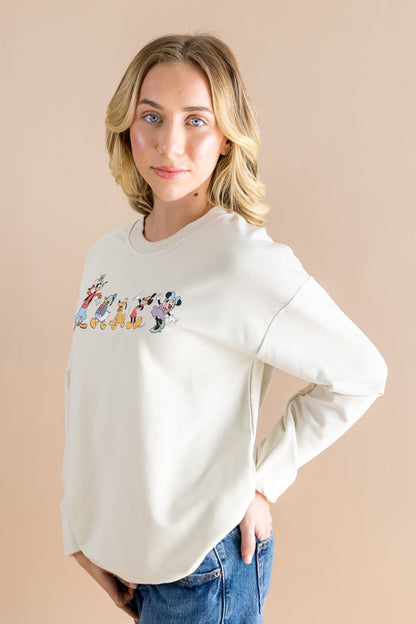 Woman wearing a cream sweatshirt with cartoon character design on a beige background