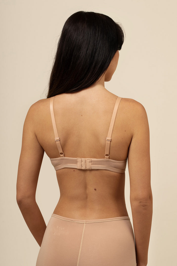 Woman wearing a beige bra and panties set against a beige background