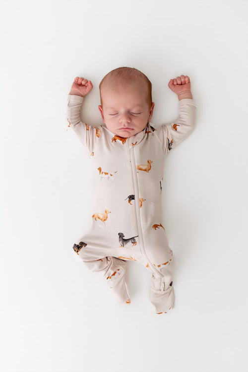 baby sleeping on a white surface wearing a zippered footie sleeper with a wiener dog pattern