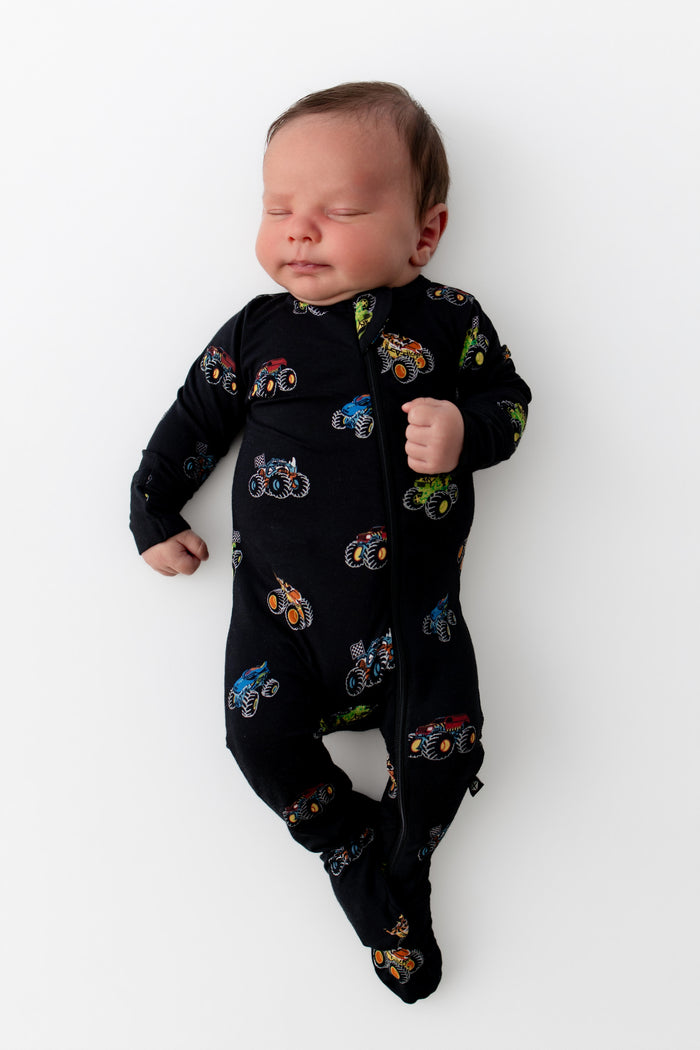 Baby sleeping in Black Zippered Footie in Monster Truck print on white background