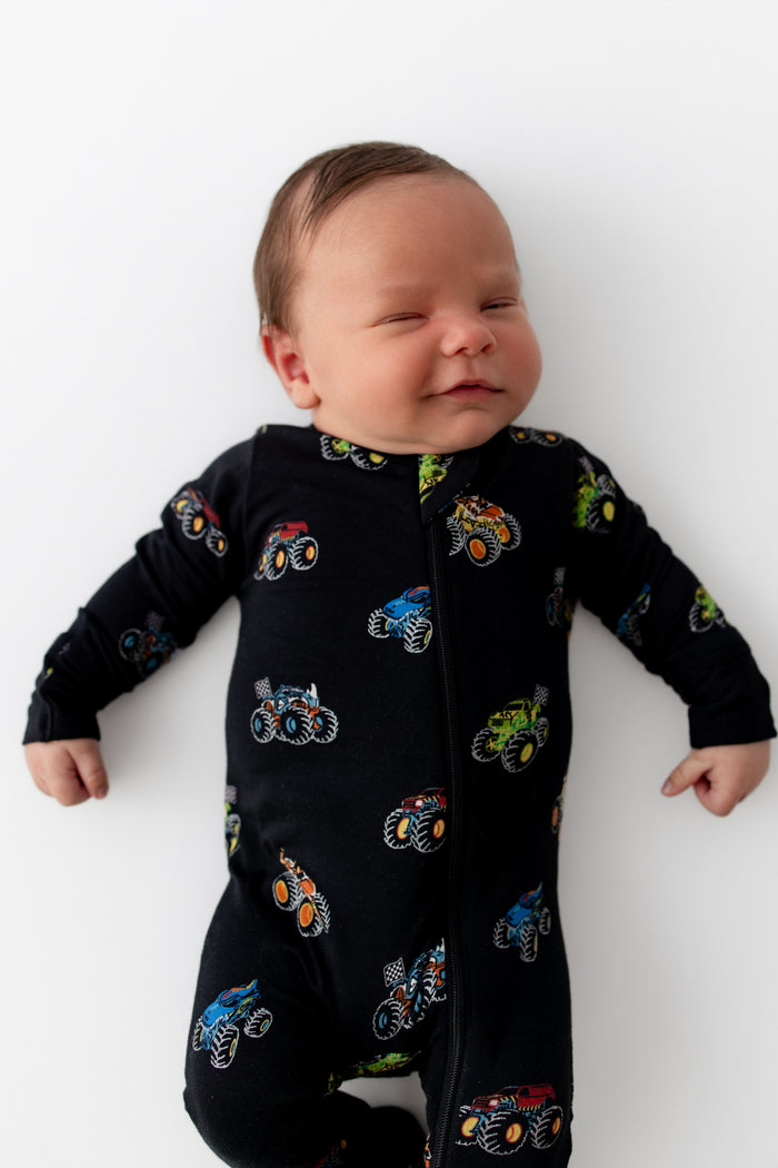 Baby wearing Black Zippered Footie in Monster Truck print on white background