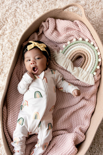 Baby yawning in a basket over a pink blanket wearing Zippered Footie in Retro Rainbow print with a retro rainbow prop